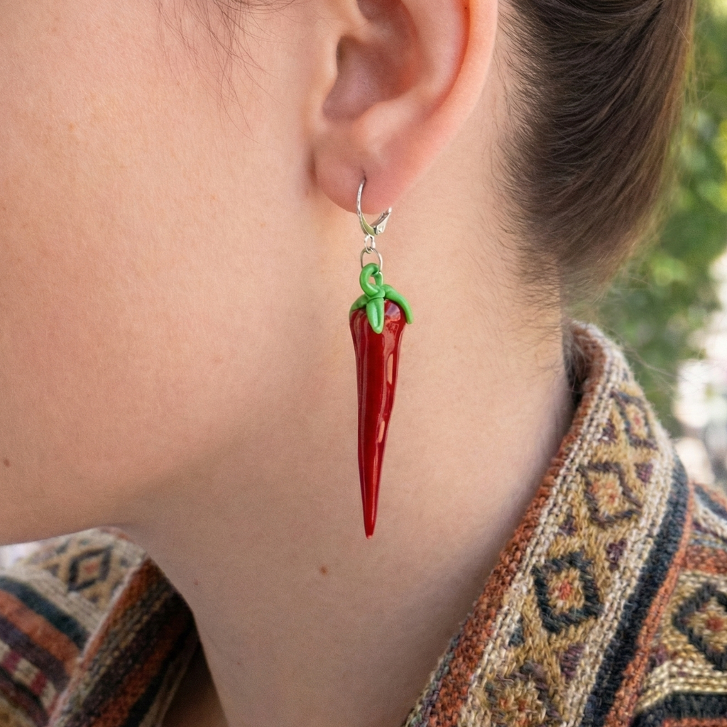Person wearing a red chili pepper earring with a blurred outdoor background