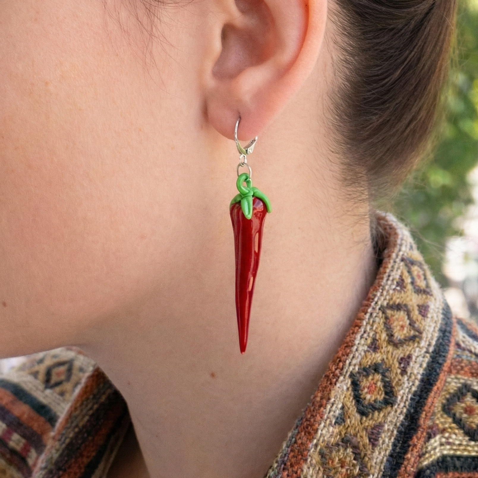 Person wearing a red chili pepper earring with a blurred outdoor background